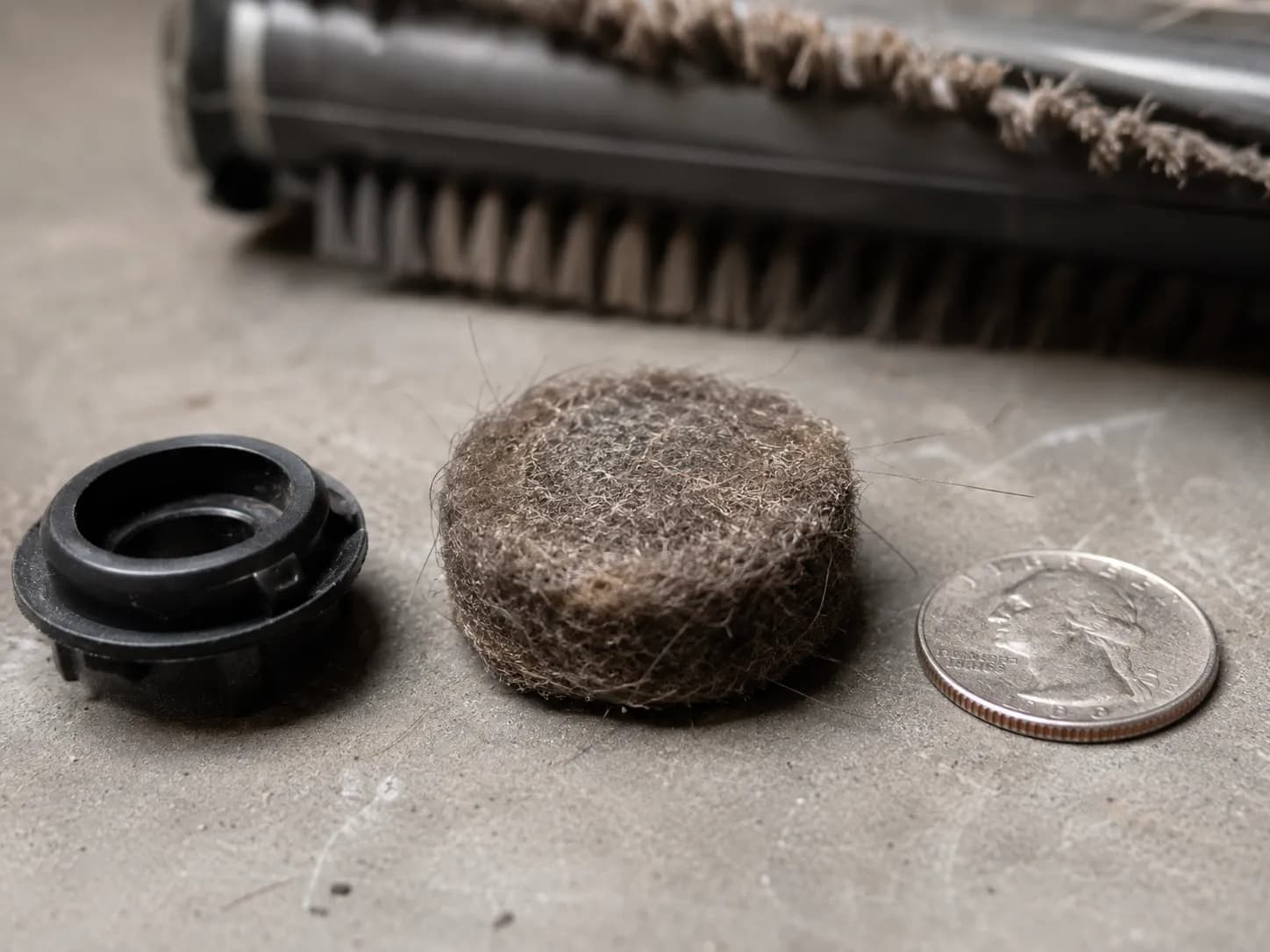 Bissell CleanView brush roll end cap beside a dense felted hair disc that stopped the roll from turning, with a quarter included for scale.