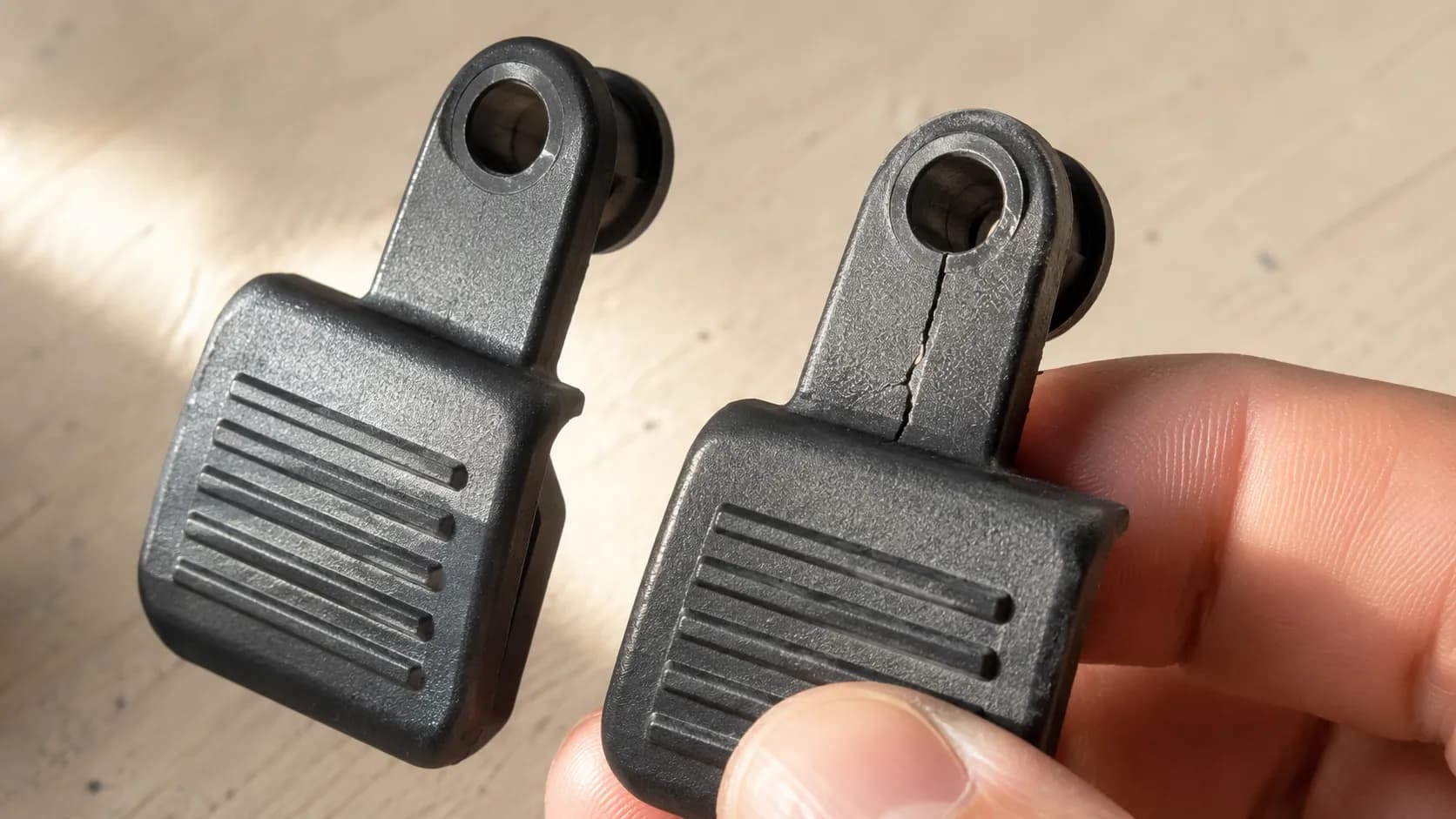 lose-up comparison of an intact and cracked Bissell PowerForce Helix handle release pedal, showing a hairline fracture around the pivot hole.
