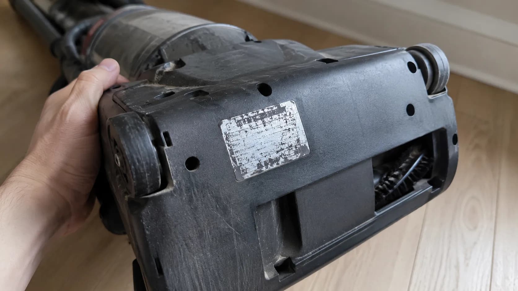 Close-up of a Bissell upright vacuum tipped back to show a worn, unreadable specification sticker on the underside of the base.