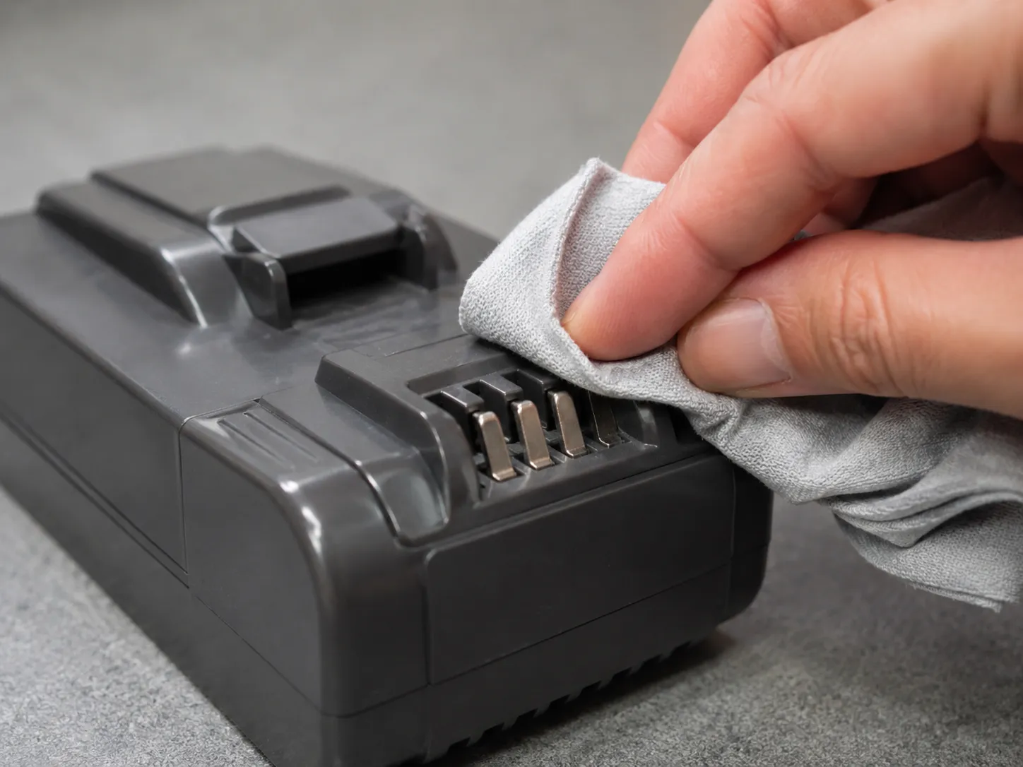 Hand wiping the exposed metal contacts on a detached cordless vacuum battery pack with a dry cloth before re-seating it.