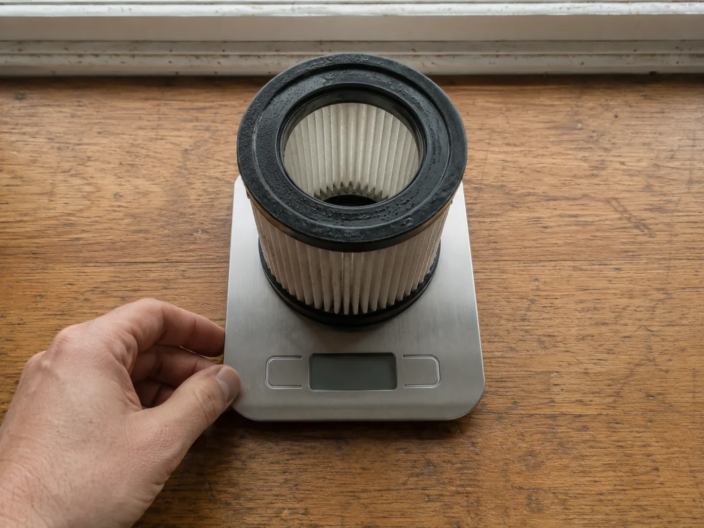 Cylindrical pleated vacuum filter placed on a digital kitchen scale to demonstrate how damp filter media can restrict airflow and reduce suction even when the dirty water tank is empty.
