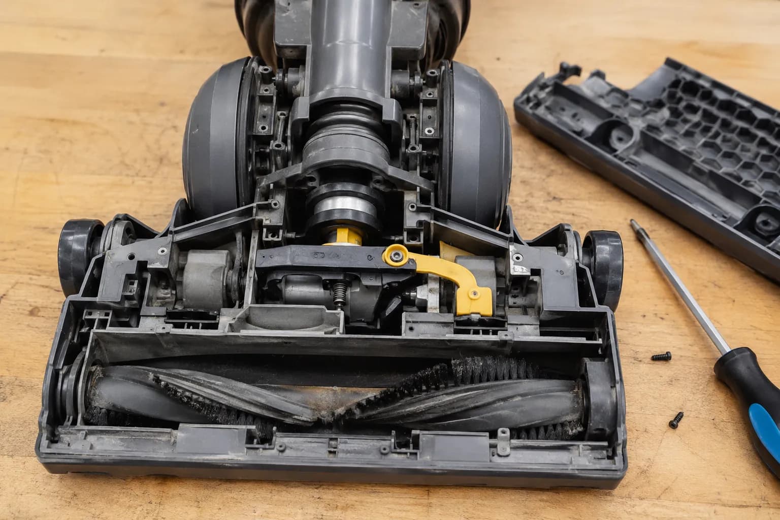 Underside of an upright vacuum with the soleplate removed, exposing the brush-roll channel, clutch and airflow diverter valve between wand and floor modes.
