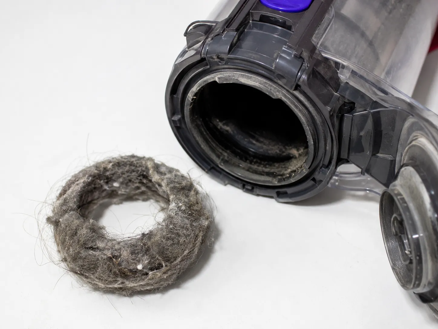 Compacted ring of lint and hair removed from a Dyson V10 bin inlet, shown beside the open inlet on a white surface.