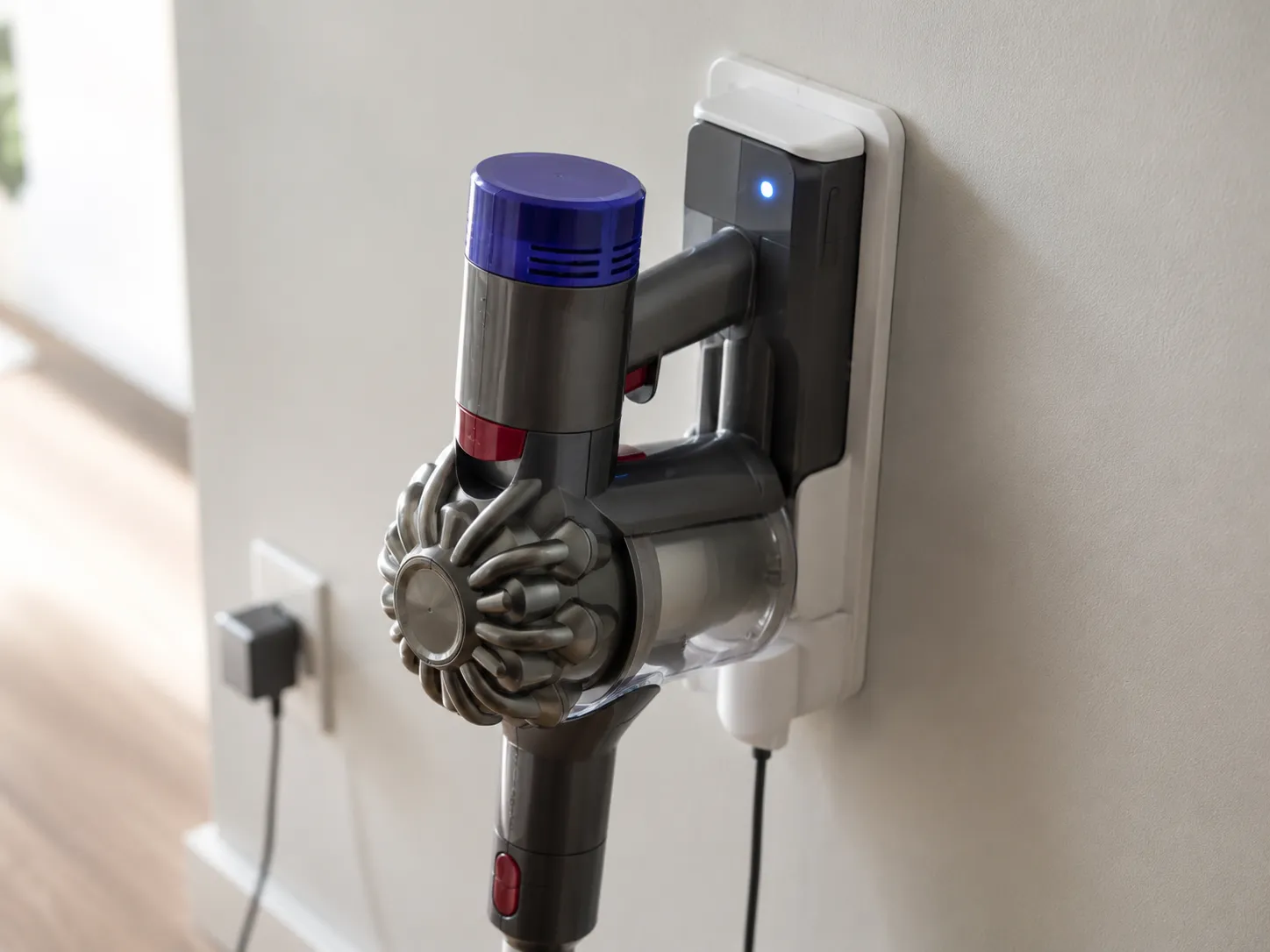 Cordless vacuum seated on a wall charging dock after an outlet swap, with a steady blue battery light showing that charging has resumed.