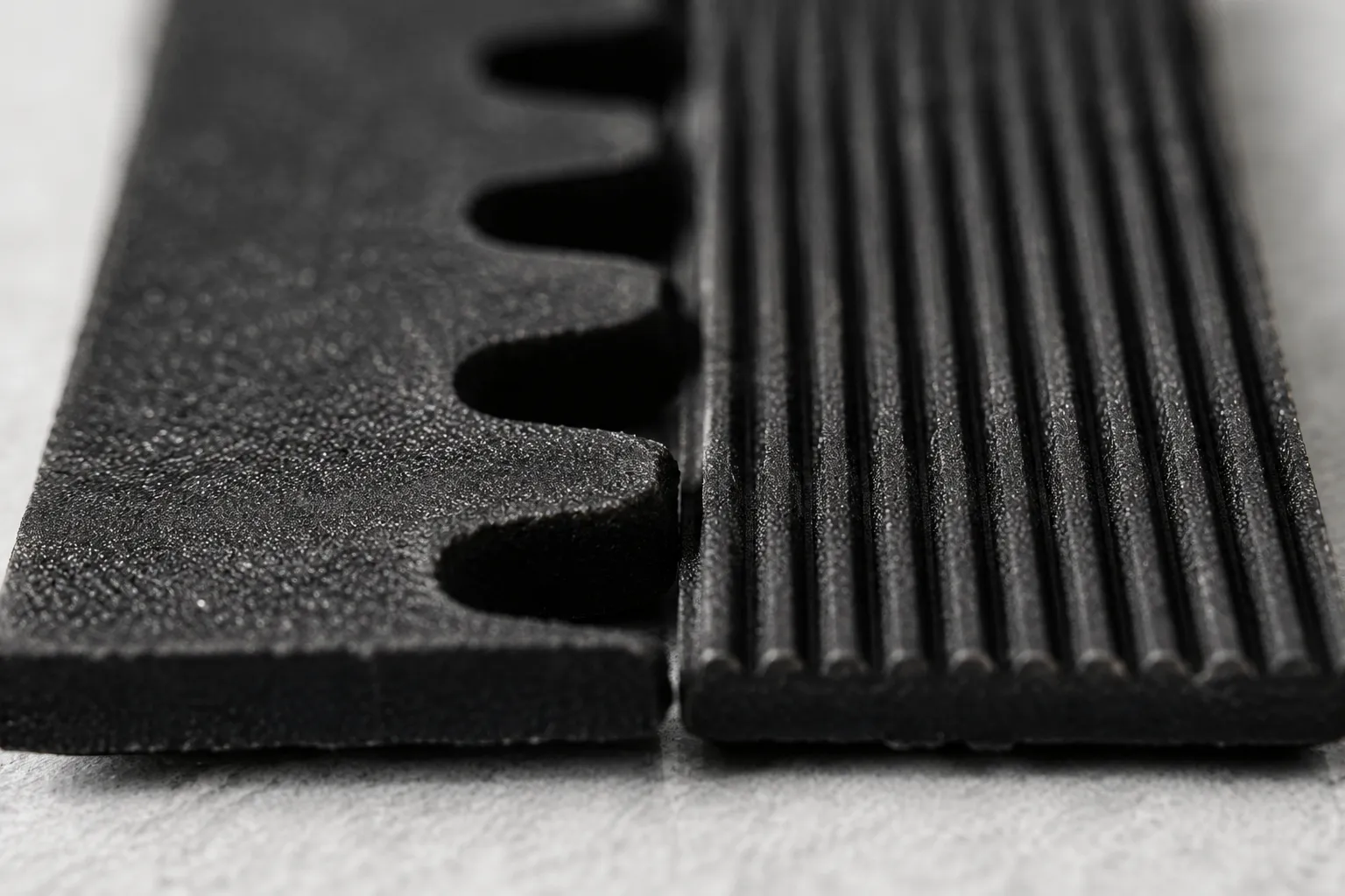 Extreme close-up of two black vacuum belts showing molded teeth on one belt and fine parallel ribs on the other, illustrating the difference between geared and grooved Shark-style vacuum belts.
