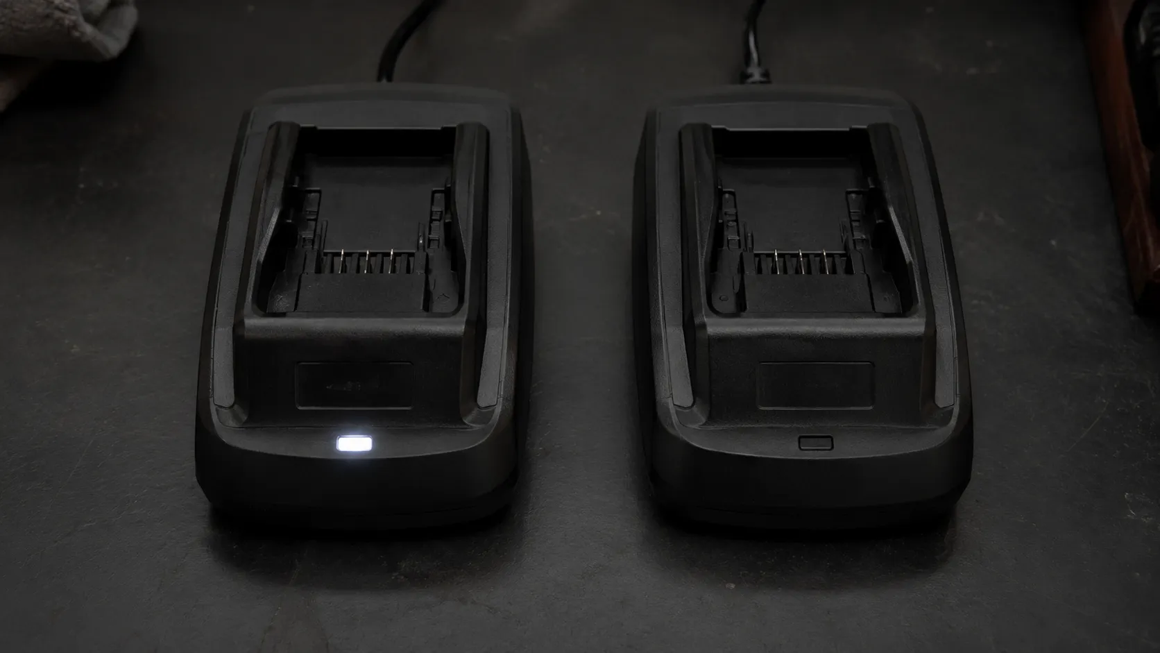 Two empty Hoover ONEPWR battery chargers plugged in side by side, with the left charger showing a faint indicator light and the right remaining completely unlit.