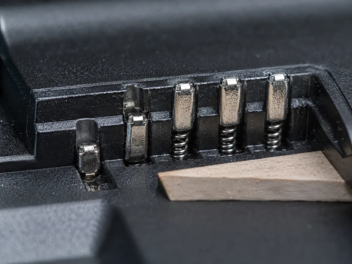 Extreme close-up of a Hoover ONEPWR charger bay showing one spring-loaded contact pin stuck below the others, causing good batteries to appear faulty.