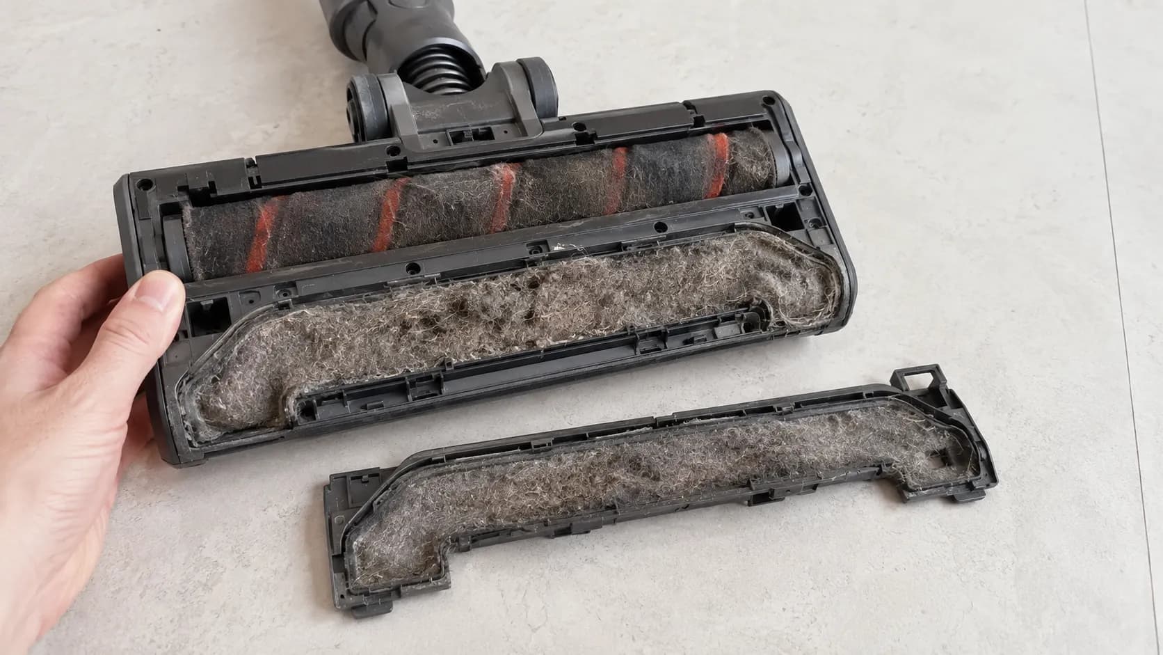 Cordless vacuum floor head with the cover removed, revealing an internal airpath channel packed solid with matted grey pet hair.