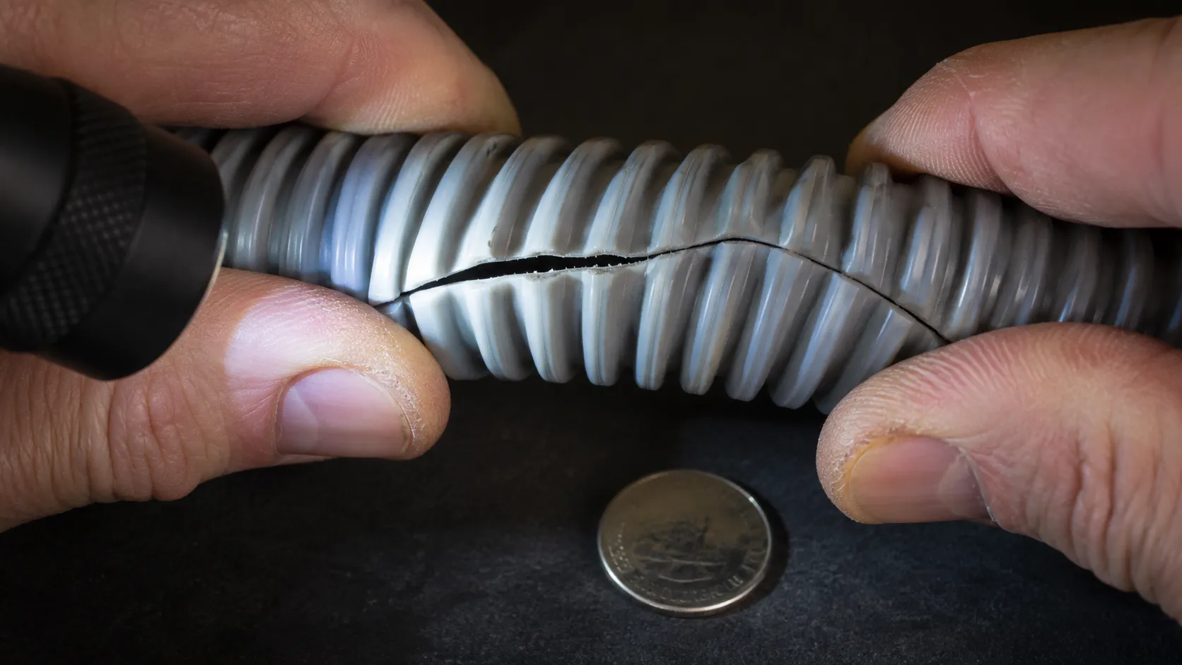 Close-up of a ribbed vacuum hose flexed open to reveal a hidden hairline split that caused major airflow loss without making an obvious sound.