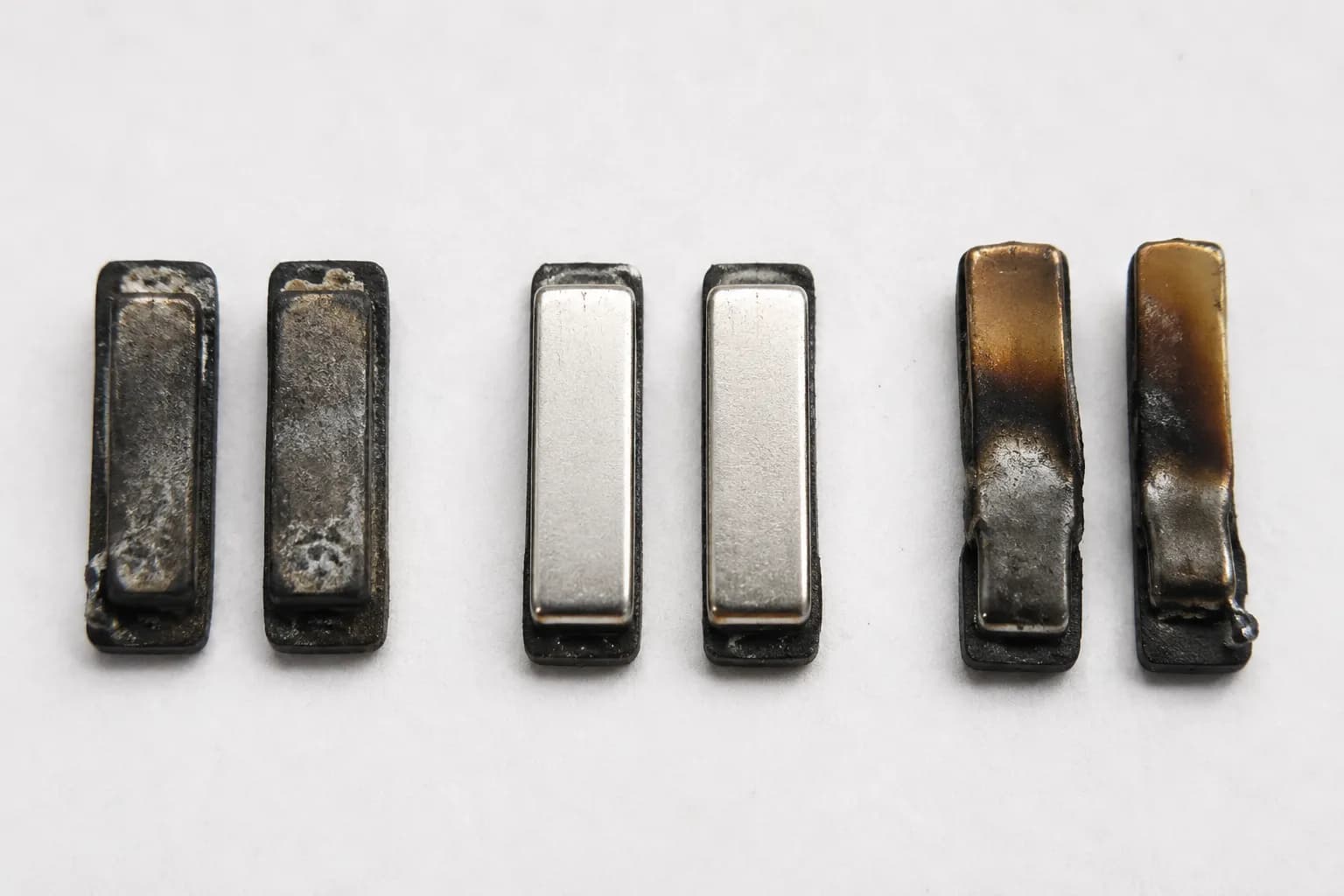 Three pairs of Roomba charging contacts showing tarnished, cleaned, and heat-damaged melted conditions side by side