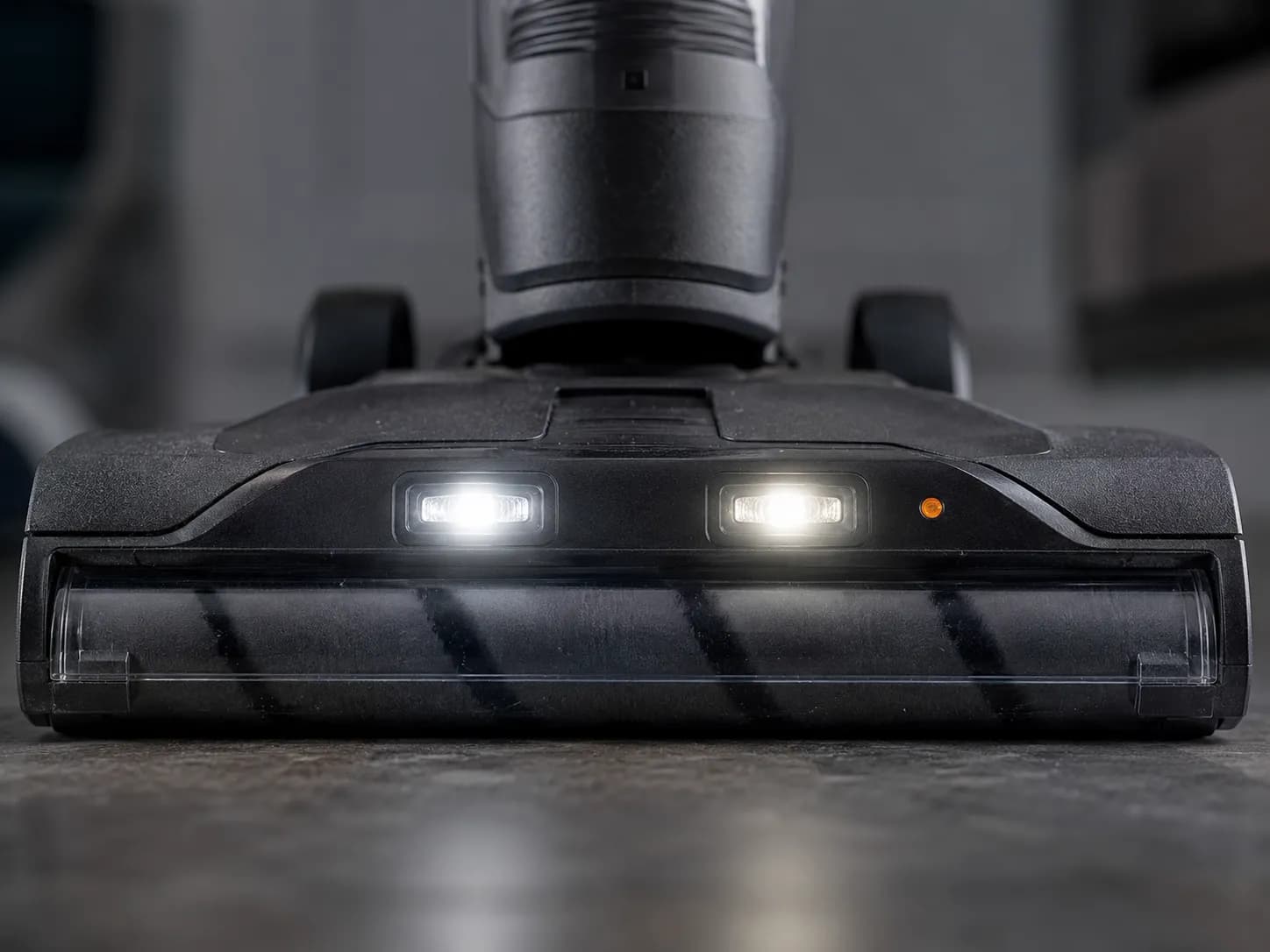 Close-up of a Shark-style upright vacuum head with front LED headlights flashing and an amber indicator light during a brush-roll jam test.
