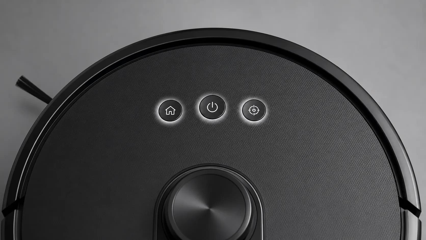 Top-down close-up of three illuminated control buttons on a black Shark-style robot vacuum, representing the Dock, Clean and Spot functions.