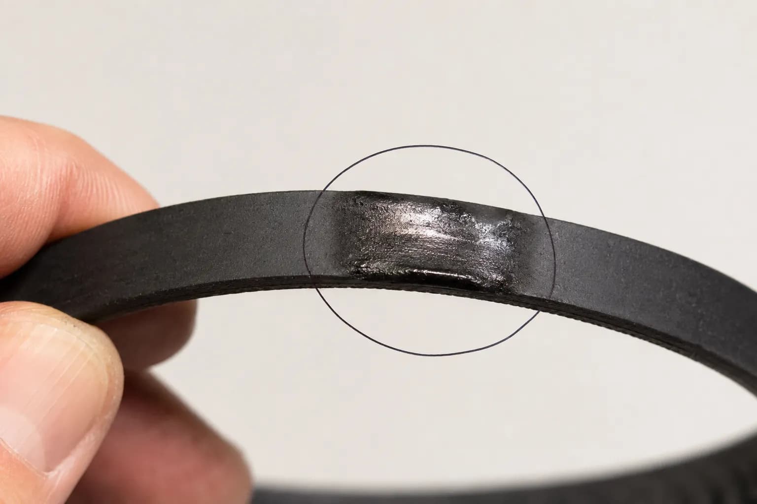 Close-up of a black Shark-style vacuum drive belt with a shiny melted flat spot circled, showing friction-burn damage from belt slippage.