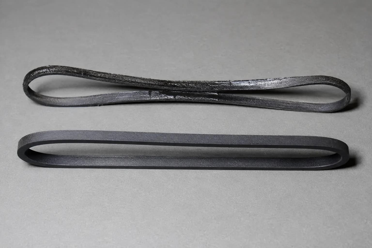 Close-up comparison of a glazed stretched Shark-style vacuum drive belt beside a new matte belt, showing belt wear and replacement signs.