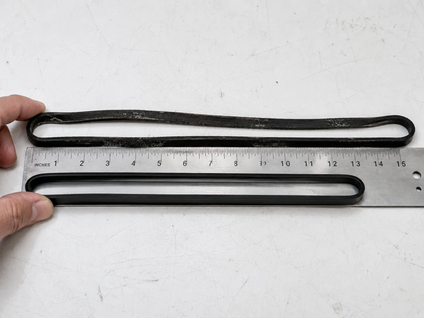 stretched old vacuum belt next to a new belt on a ruler showing the size difference