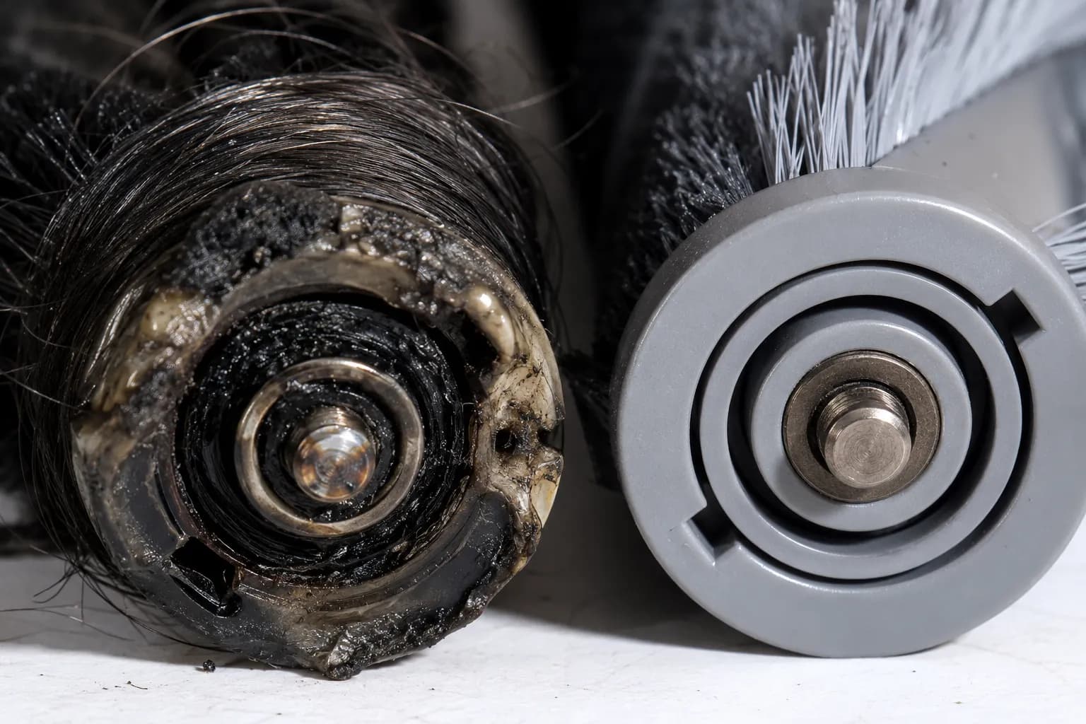 Close-up comparison of two vacuum brush-roll ends, showing a melted discolored bearing cap with wrapped hair beside a clean intact brush-roll end.