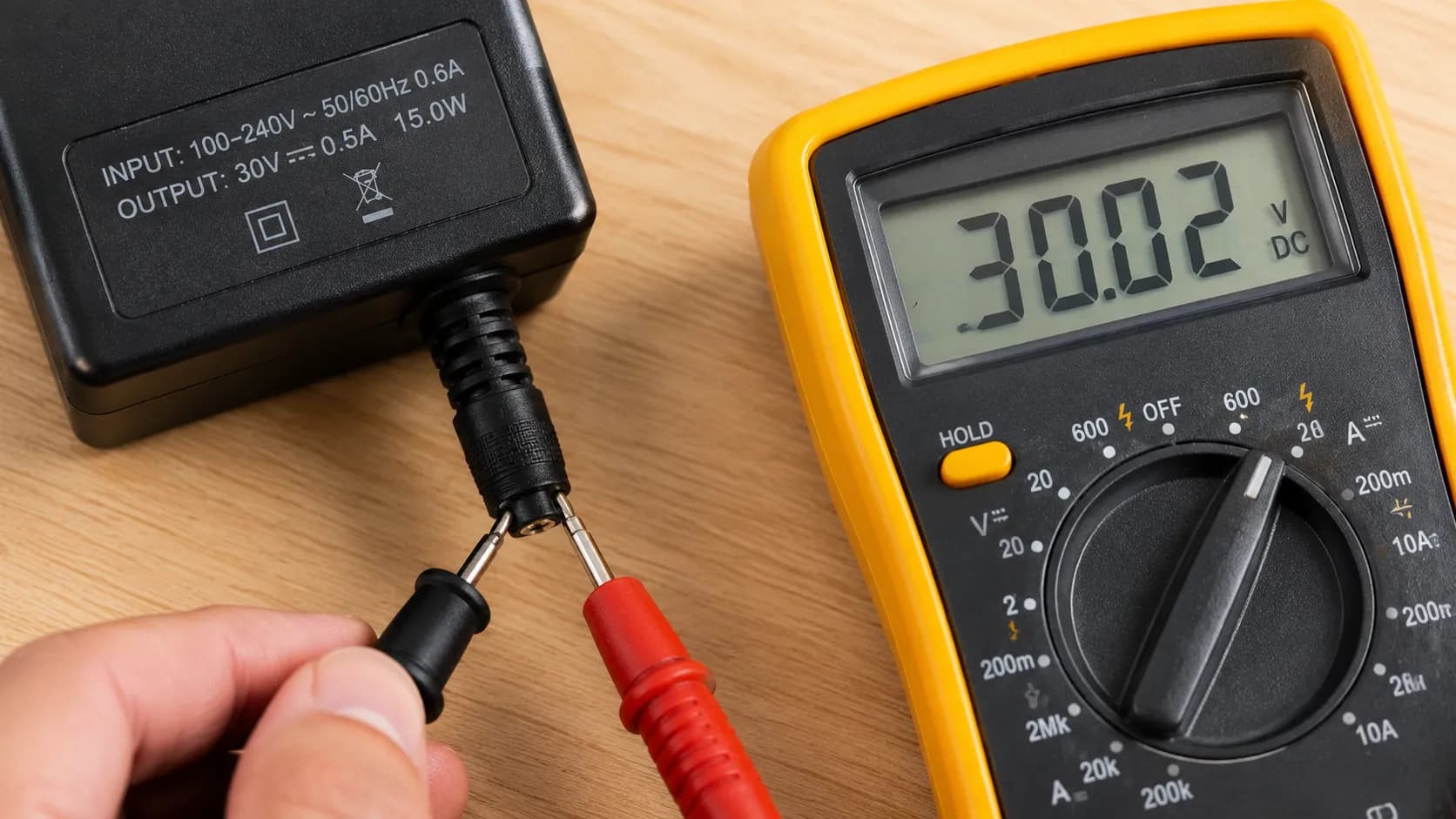 Close-up of a digital multimeter testing a vacuum charger output voltage beside the charger's printed output rating label to compare measured voltage with manufacturer specifications.