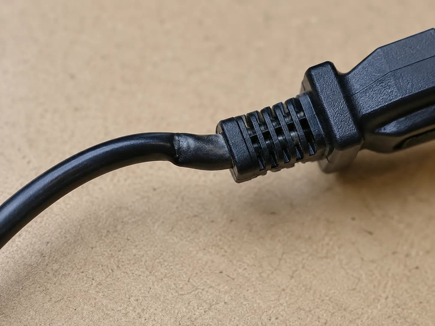 Close-up of a black vacuum power cord bent near the molded plug, showing the stressed kink point checked during a wiggle test.