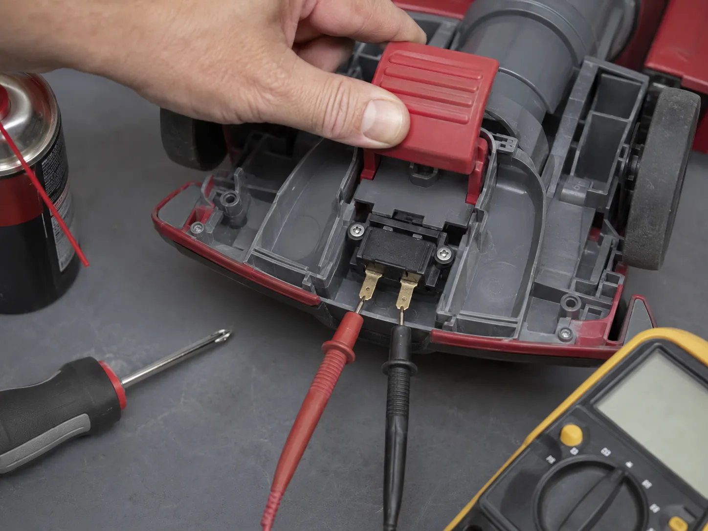 Multimeter testing the power switch terminals inside an opened Bissell CleanView Swivel Pet foot housing while the red pedal is held down.