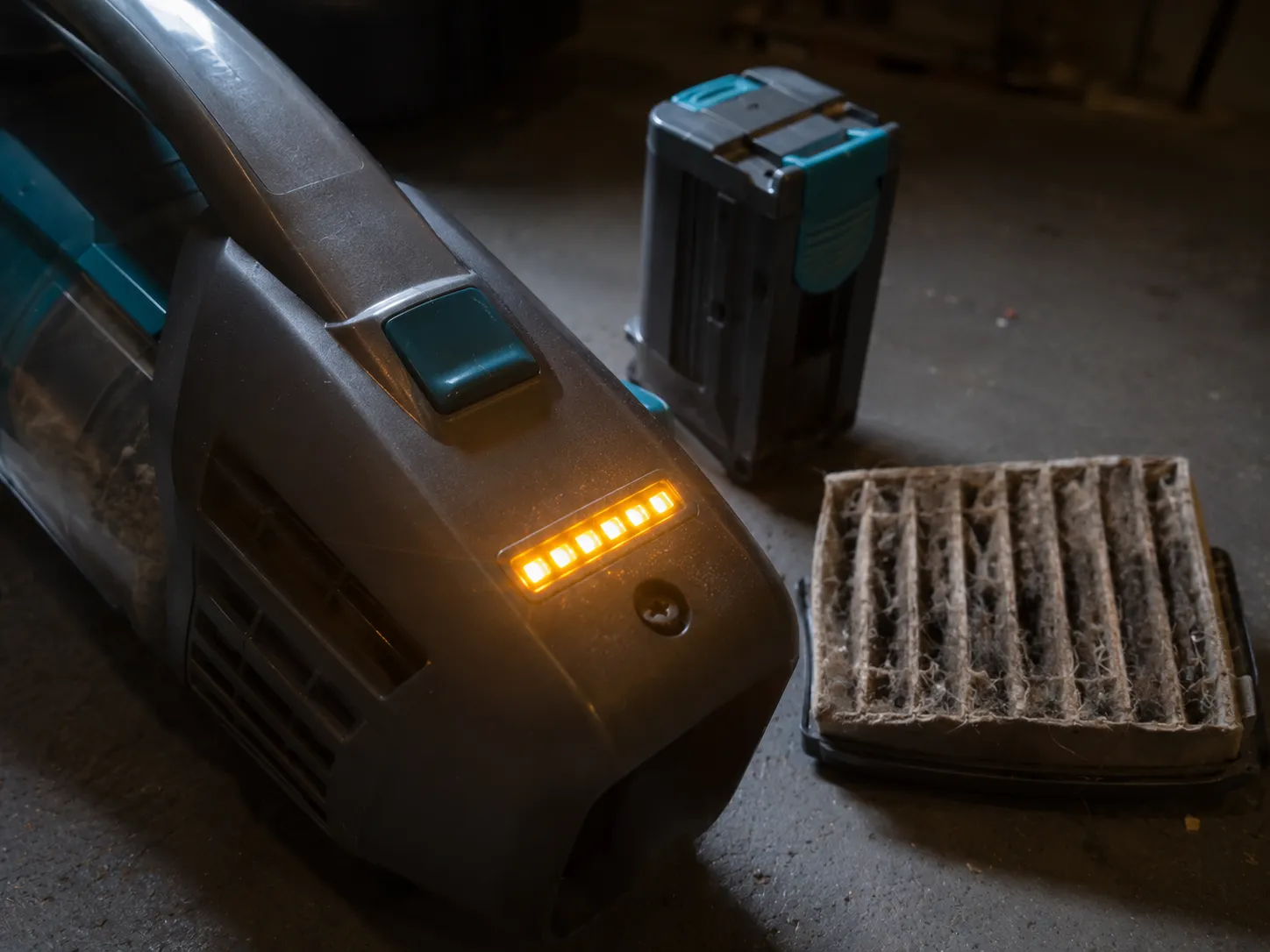 Bissell CleanView XR Pet cordless vacuum with its amber LED array flashing beside a deliberately clogged filter and detached battery pack.
