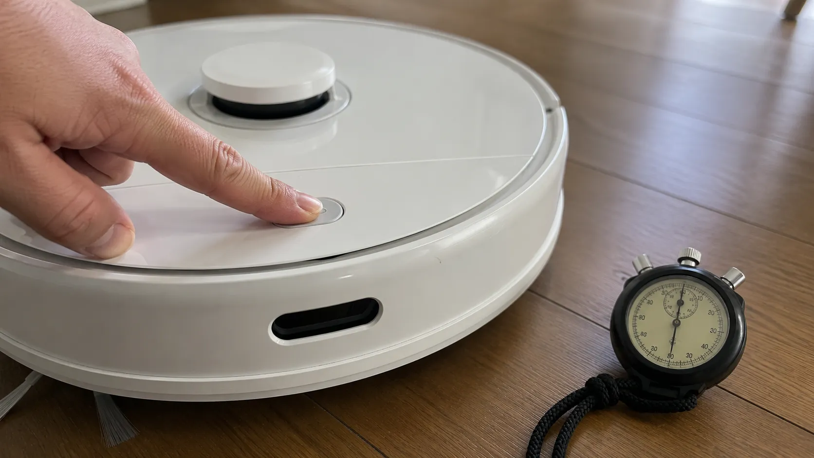 Close-up of a robot vacuum reset button being held beside a stopwatch, showing that the reset beeps occur after 46 seconds and releasing at 30 seconds does not trigger a reset.