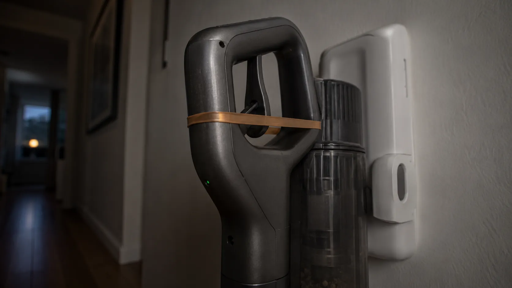 Cordless vacuum charging on a wall dock with a rubber band holding the trigger pressed, showing why this temporary trigger fix can be unsafe.