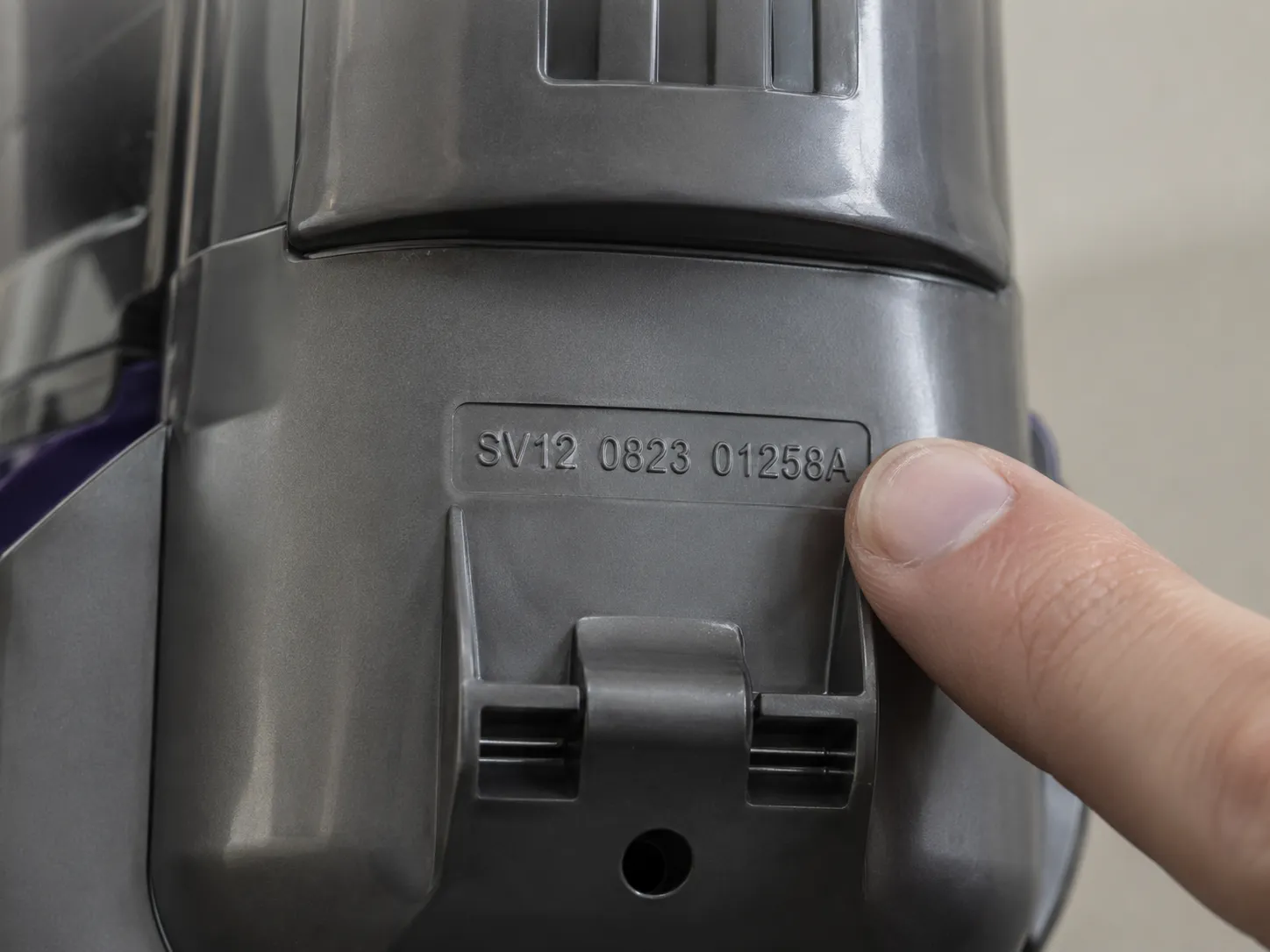 Close-up of a Dyson V11-style cordless vacuum rear housing showing the stamped SV reference code with a fingertip pointing beside it.