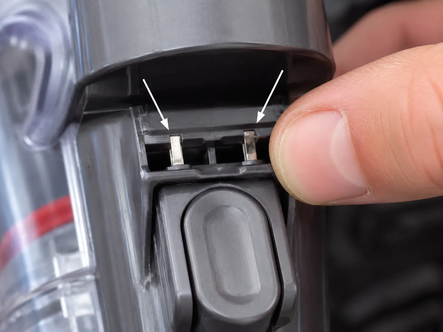 Macro close-up of Dyson V6-style brush power contact tabs above the bin lever, with a fingertip reseating a slightly bent metal tab during repair.