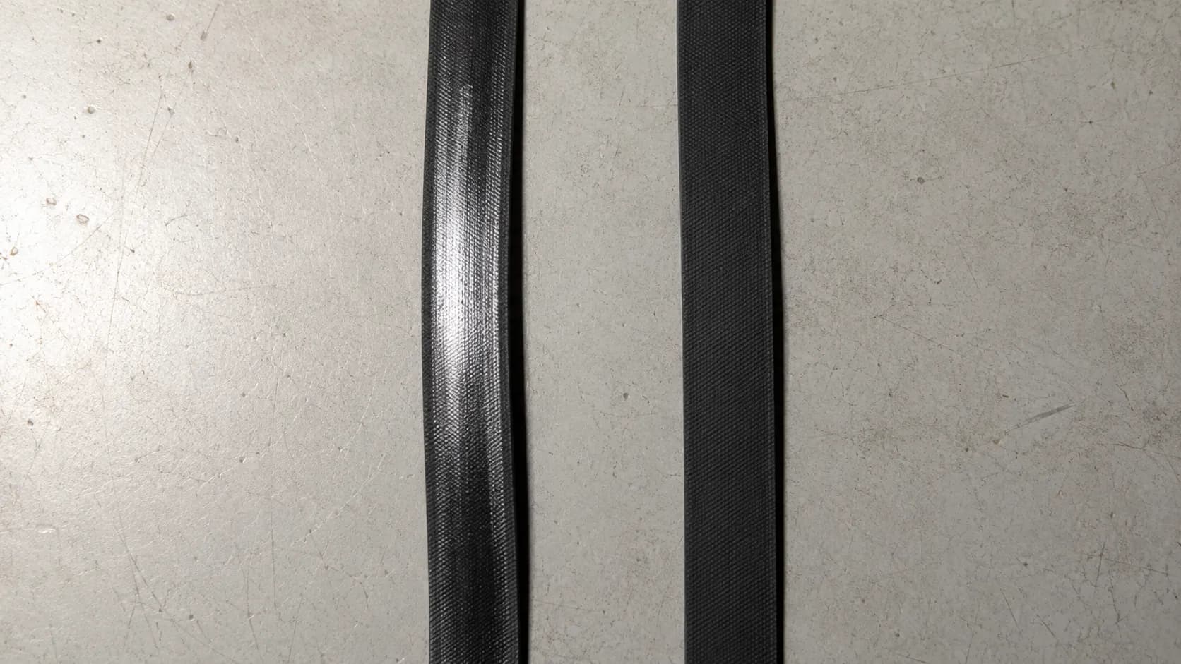Close-up comparison of an overheated vacuum drive belt with a faint glossy glazed surface beside a uniformly matte undamaged belt.