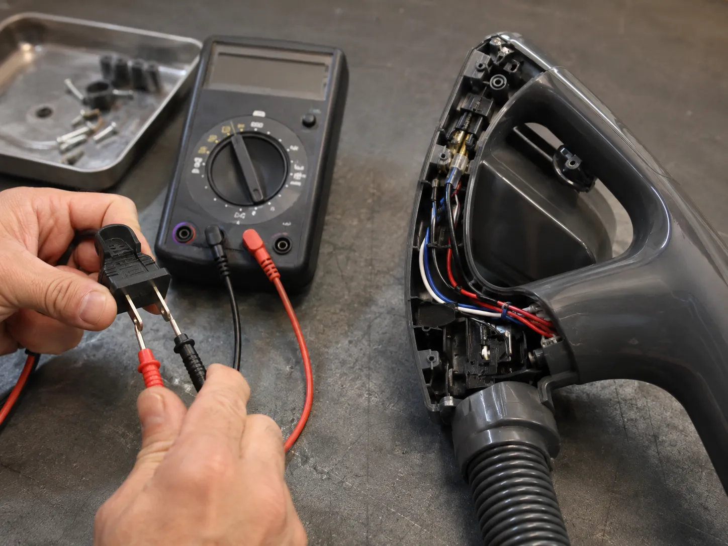 Multimeter probes testing continuity across an unplugged vacuum plug while the opened handle assembly and exposed wiring lie on a workshop bench.