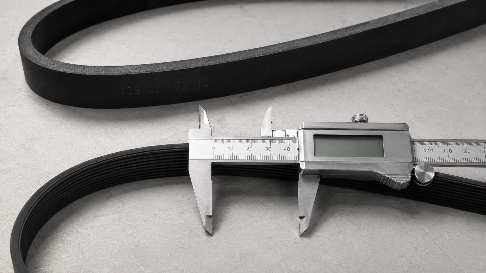 Two confirmed Kenmore-style vacuum belts on a work surface, with a flat upright belt above and a grooved canister belt below measured with digital calipers.