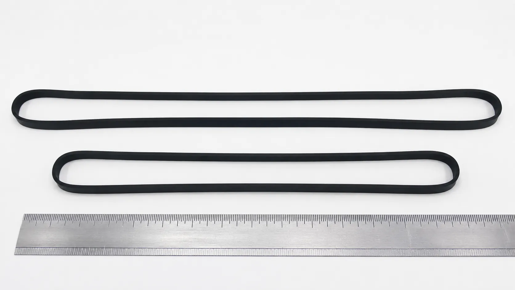 Two flat vacuum belts laid beside a steel ruler, showing one belt stretched approximately 1.3 cm longer than the other despite both appearing intact.
