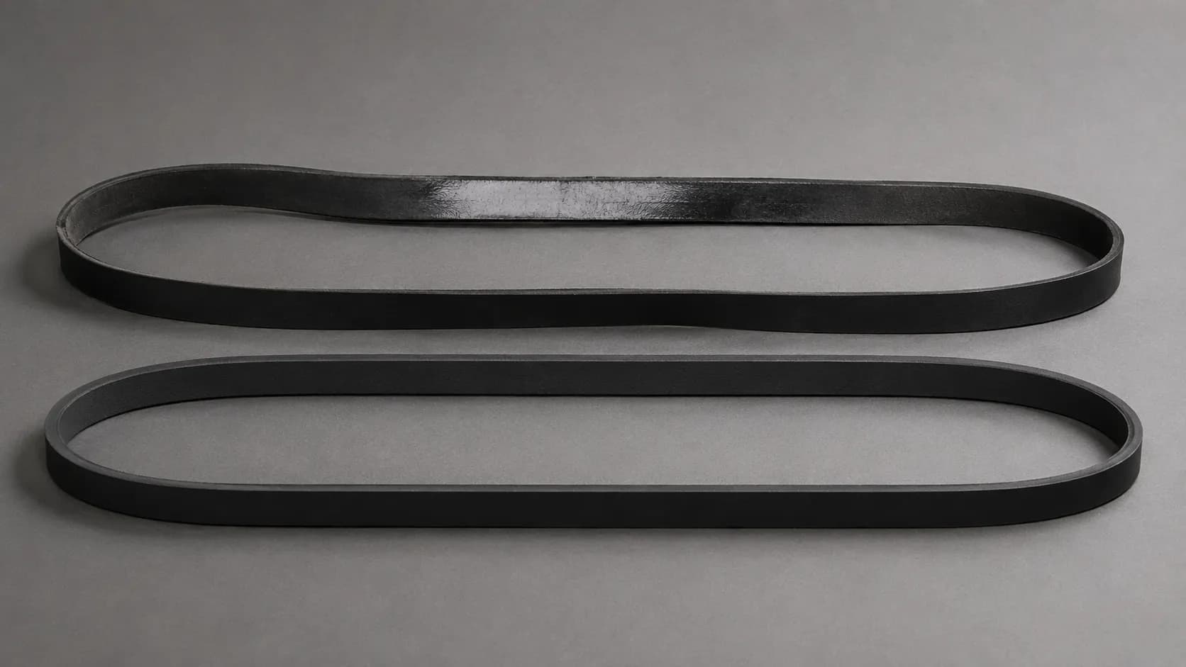 Two matching vacuum belts from the same machine shown 14 months apart, with the older belt visibly glazed and slack beside a newer matte belt with even tension.