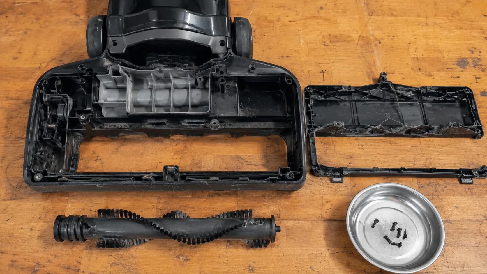 Open vacuum cleaner base with the bottom cover and brush roll removed, showing an empty drive cavity with no belt or pulley to replace.