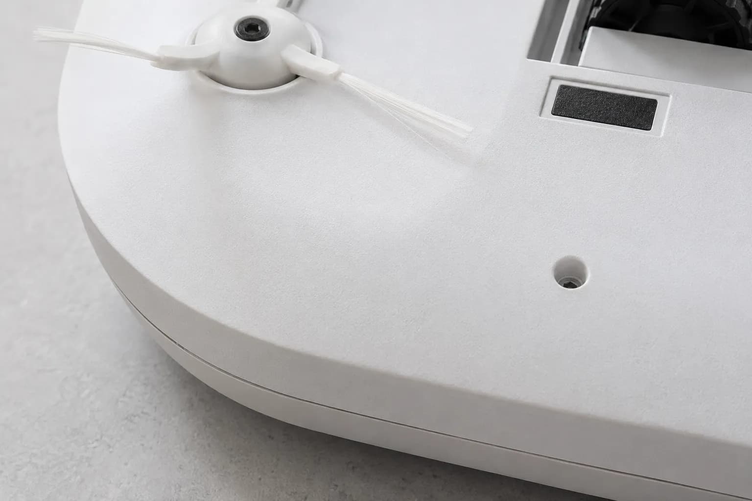 Close-up of a non-modular robot vacuum underside showing a continuous moulded housing near the side brush with no visible seam, panel line or screw.