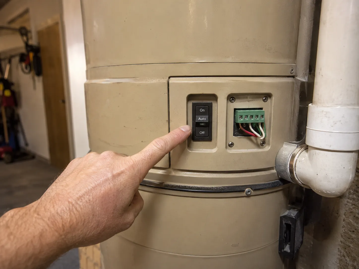 NuTone VX550 central vacuum power unit on a garage wall with a hand pointing to the Auto switch setting beside the low-voltage terminal block.