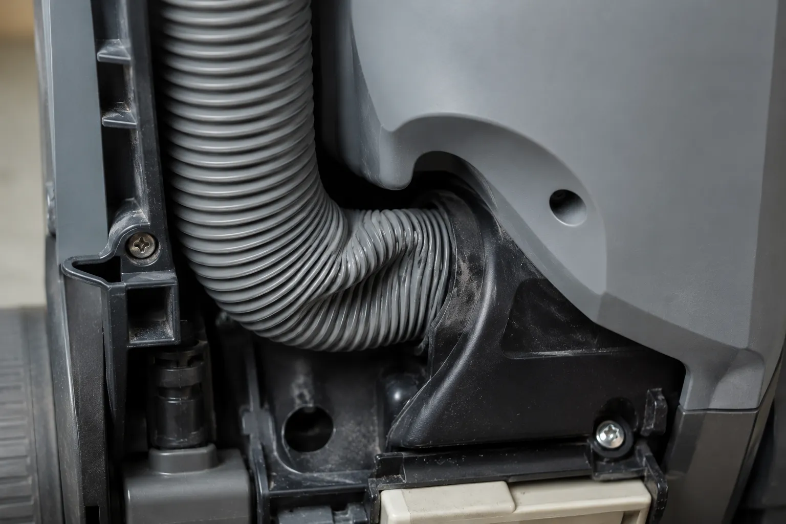 Close-up of a grey vacuum hose pinched flat between plastic housing panels, creating an airflow blockage that can mimic a failed motor.