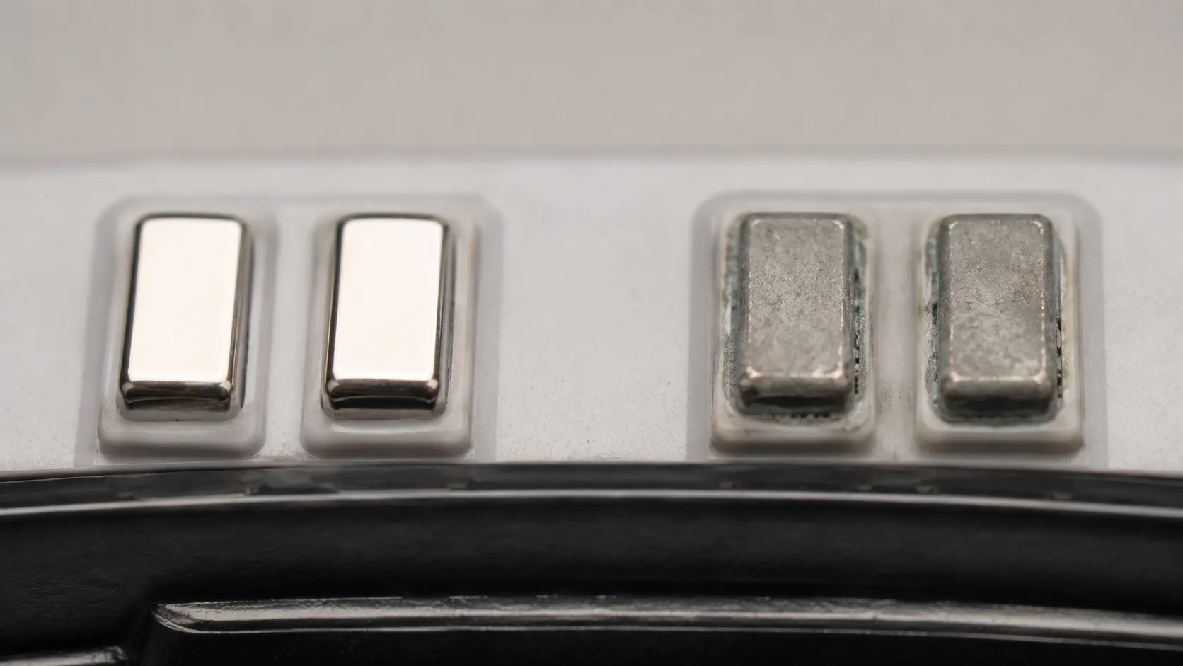 Macro comparison of robot vacuum charging contacts, showing one clean and reflective pair beside another dulled by a grey oxide film and light edge corrosion.