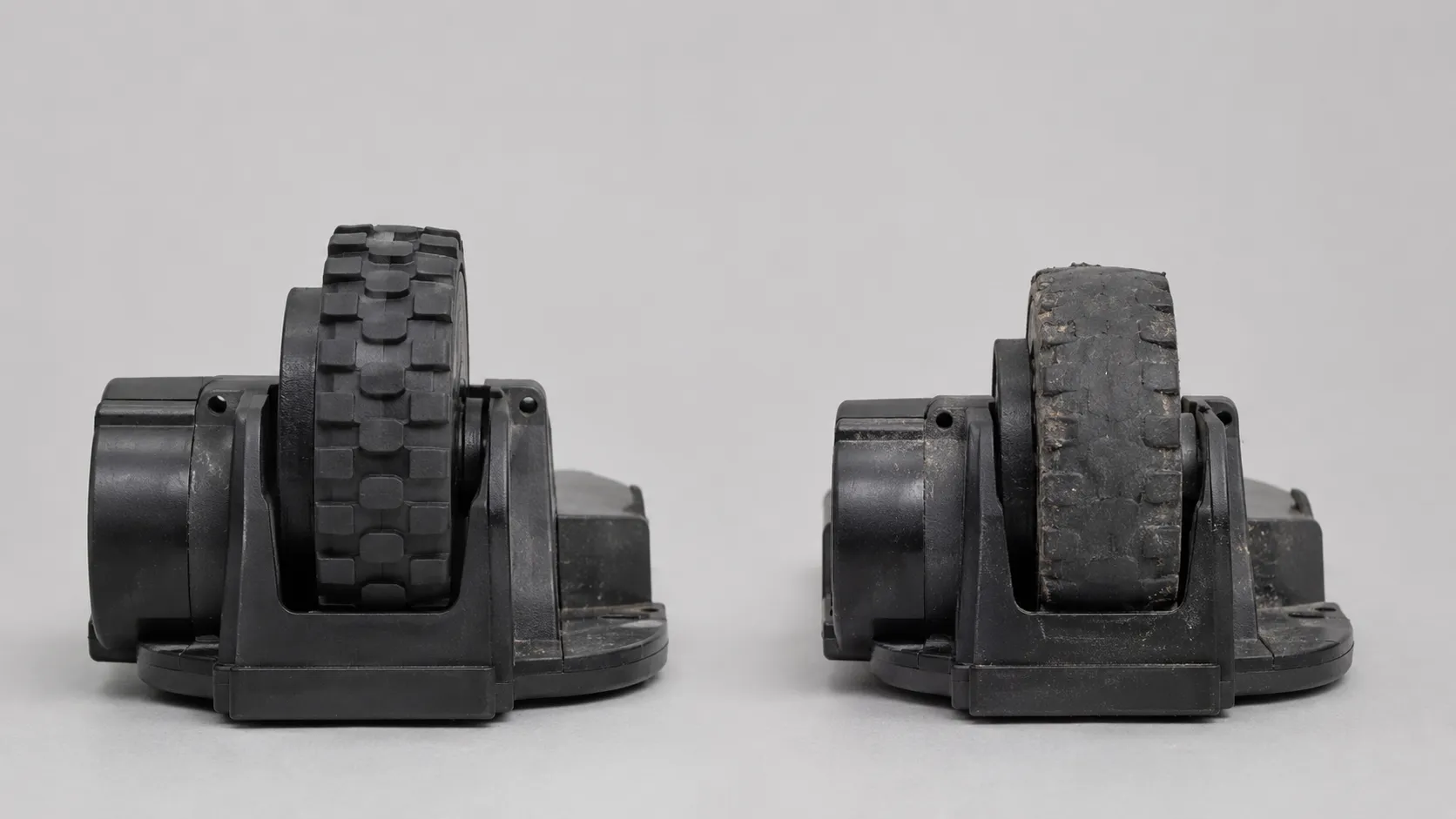 Close-up comparison of two robot vacuum drive wheel modules, showing an intact tread on the left and a heavily worn, damaged wheel on the right.