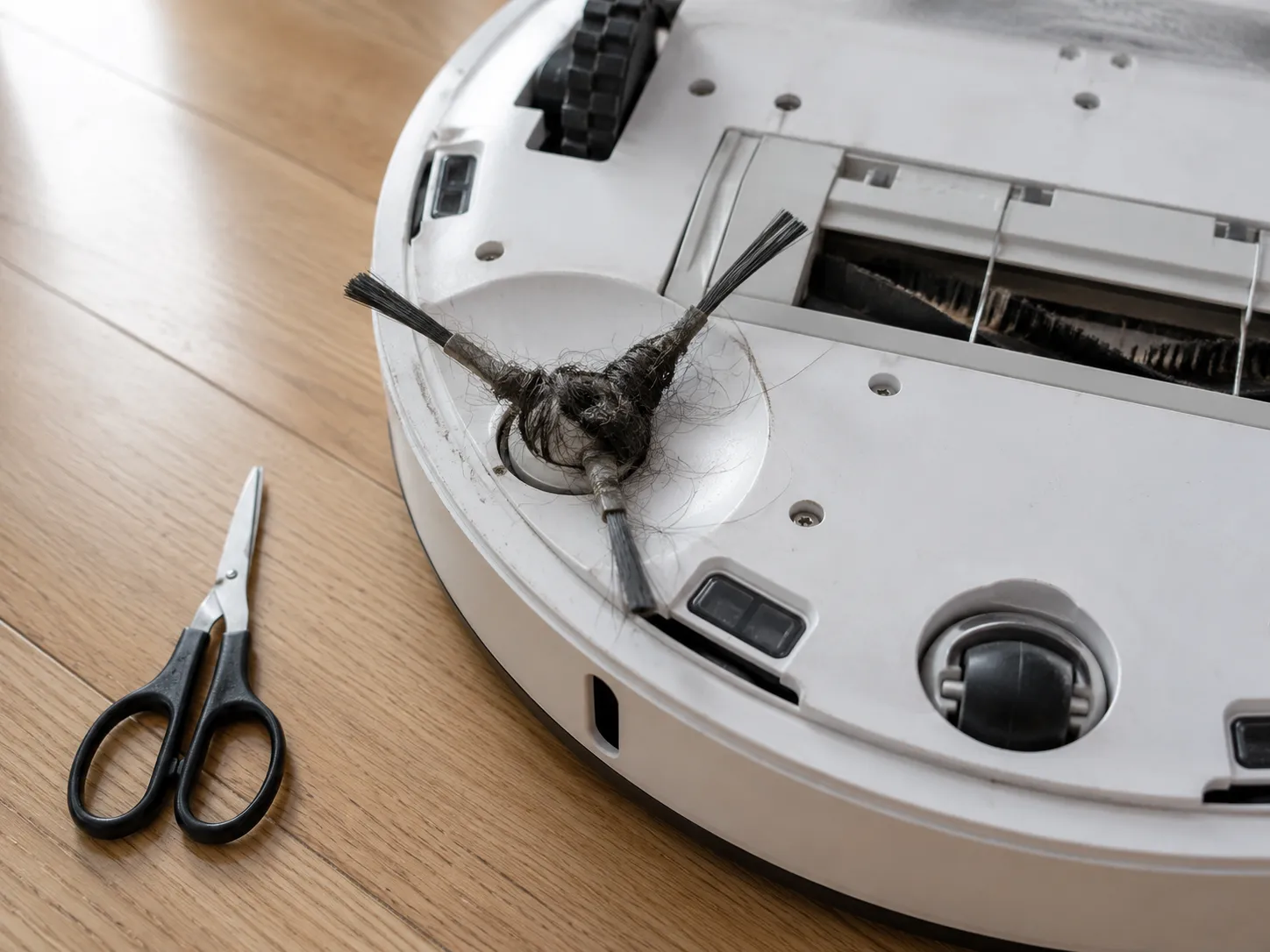 robot vacuum flipped over showing a side brush tangled with hair