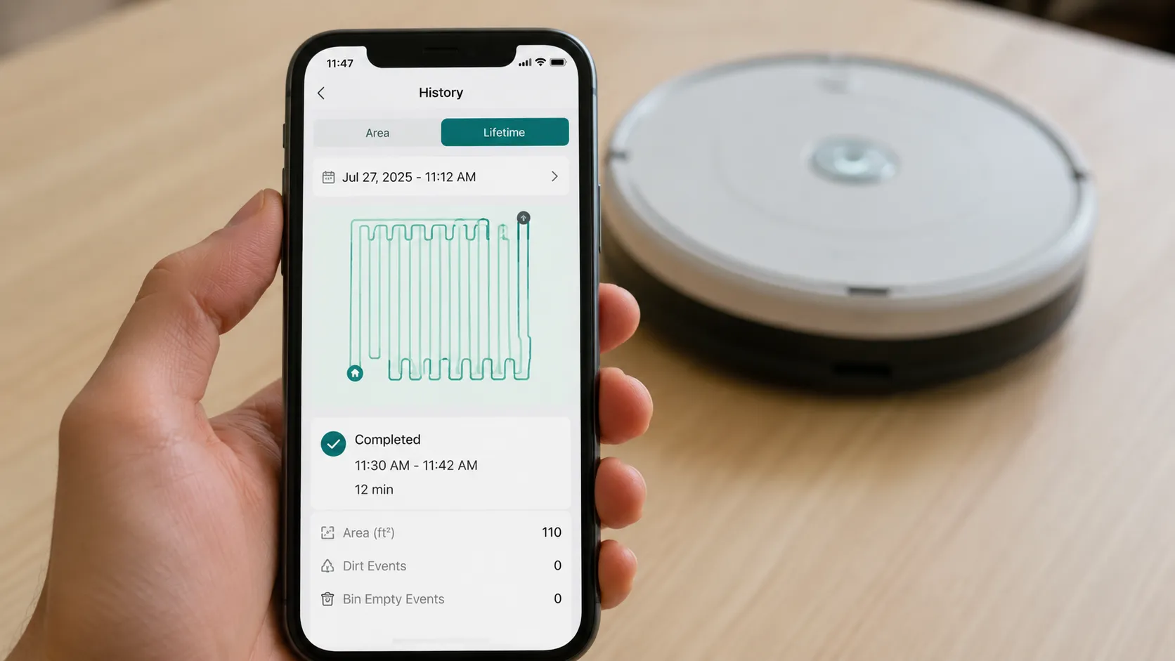 Smartphone displaying a robot vacuum cleaning mission history with a completed run, repeated reverse movement pattern on the map, and no error notifications while a Roomba 675 sits blurred in the back
