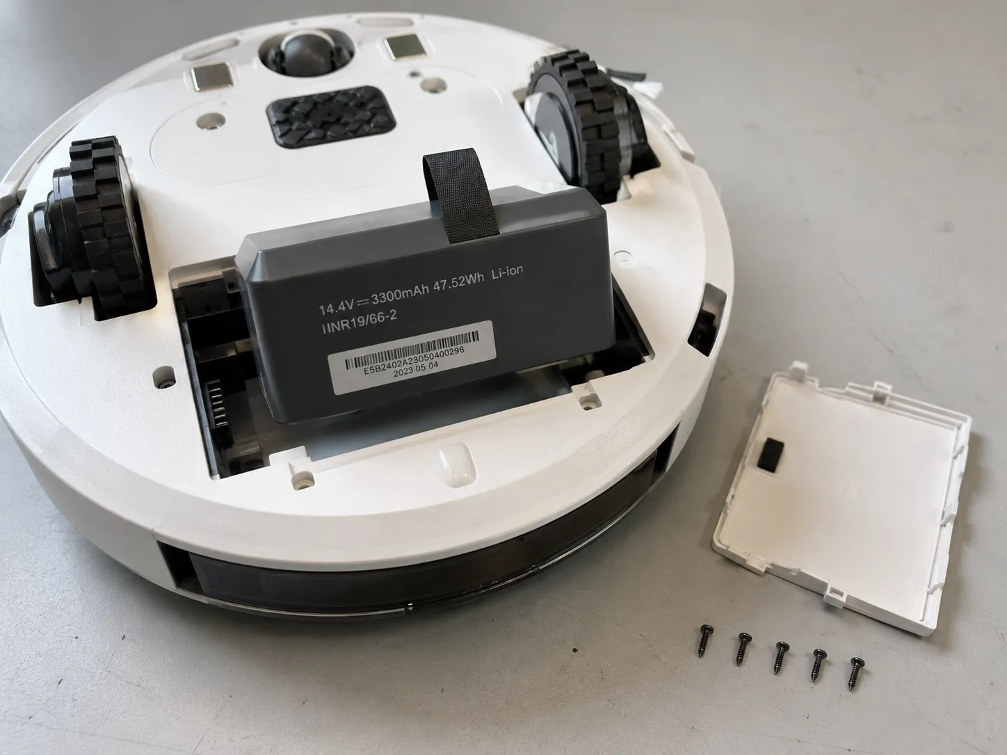 Roomba e5 with its battery compartment open, the lithium-ion pack lifted halfway out and the battery date code visible.