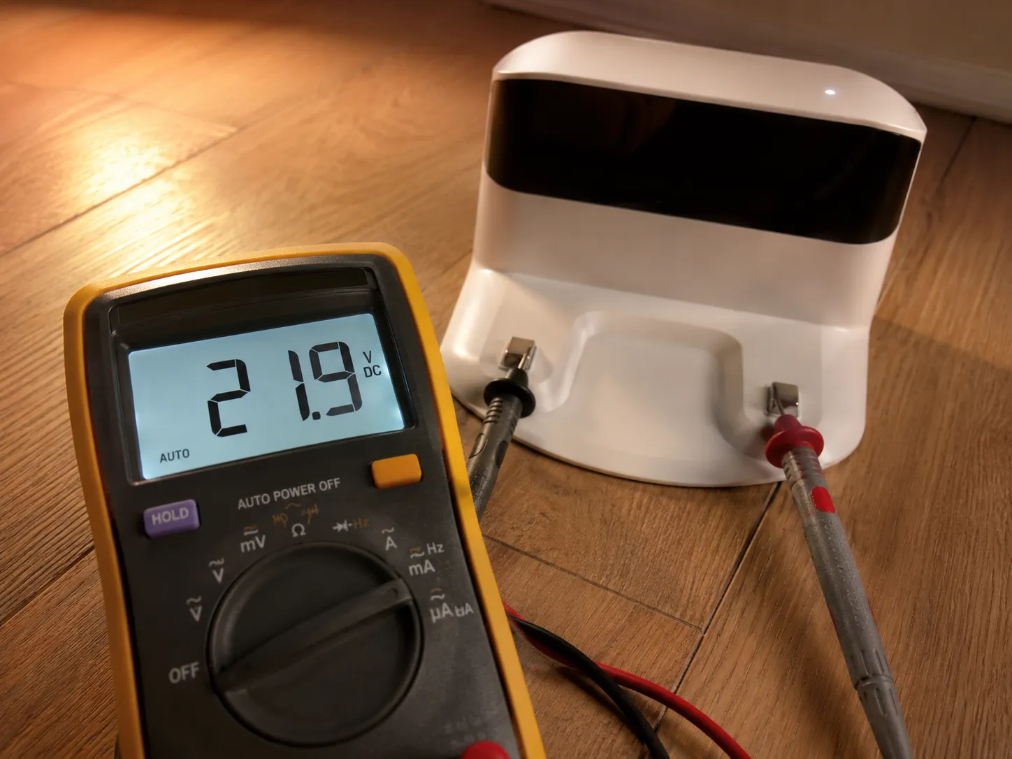 Digital multimeter reading 21.9 volts while probing the charging contacts on a Roomba Home Base dock.