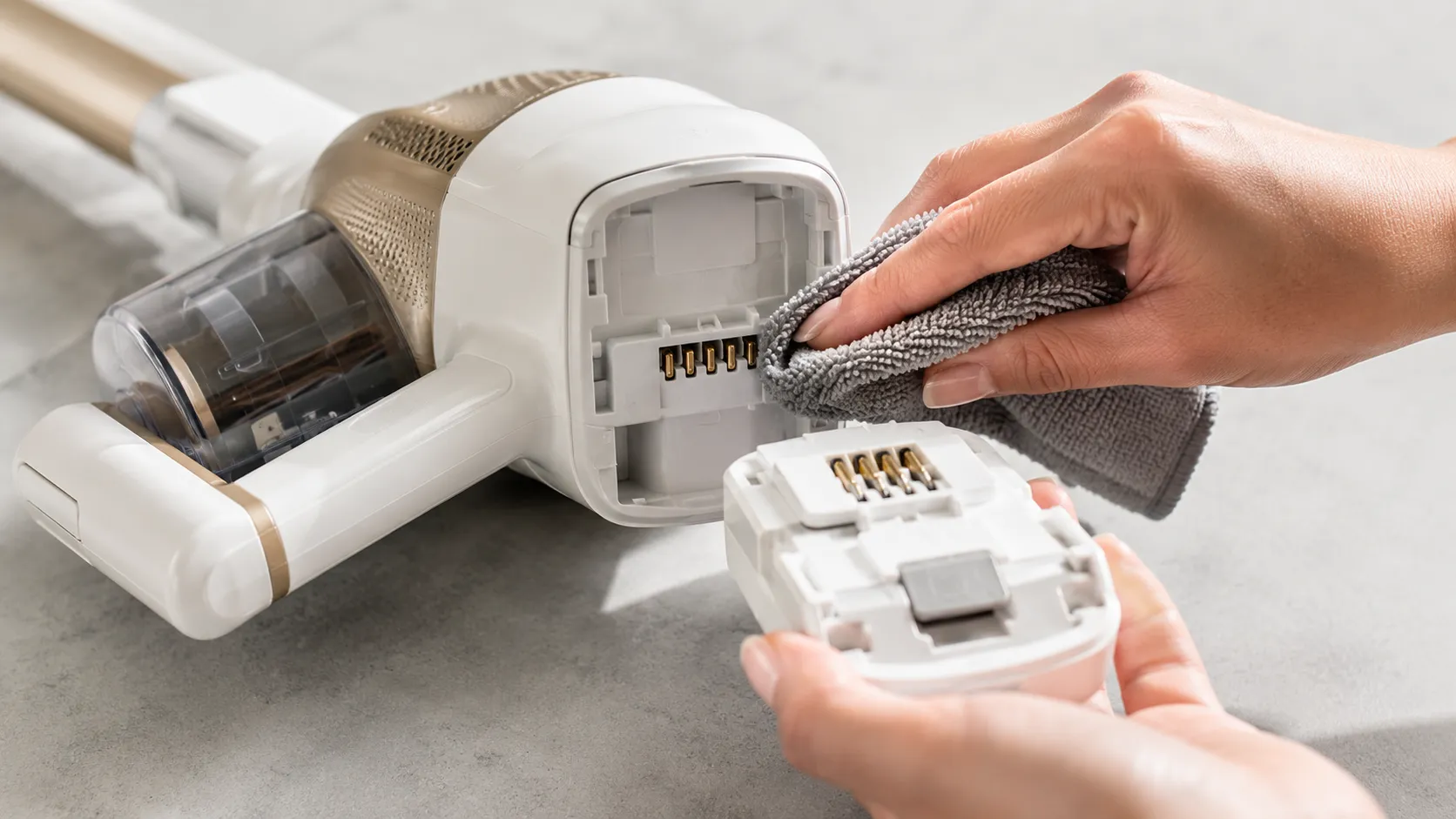 Shark cordless vacuum with battery removed as metal charging contacts are cleaned with a microfiber cloth before reseating