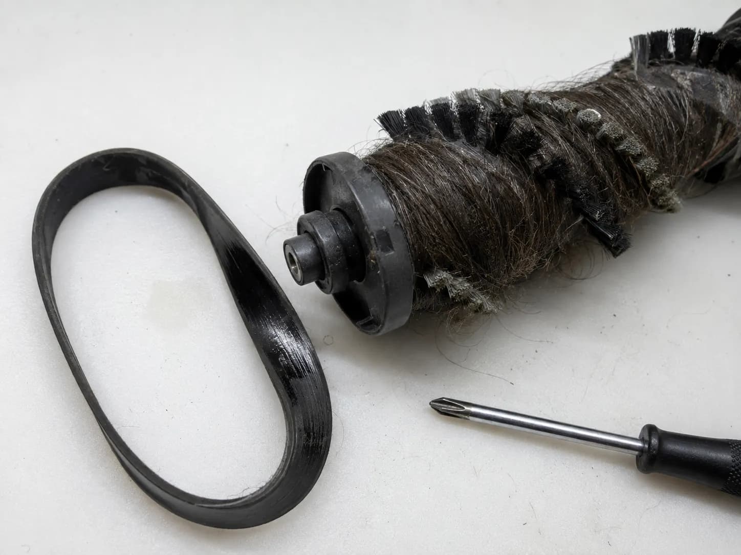 Worn Shark vacuum drive belt beside a brush roll wrapped with hair and lint.