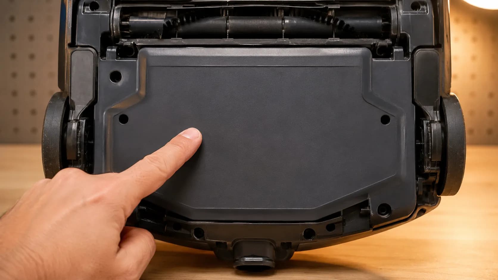 Underside of a Shark-style upright vacuum showing a blank motor housing area with no reset button present, while a hand points to where owners may expect one.