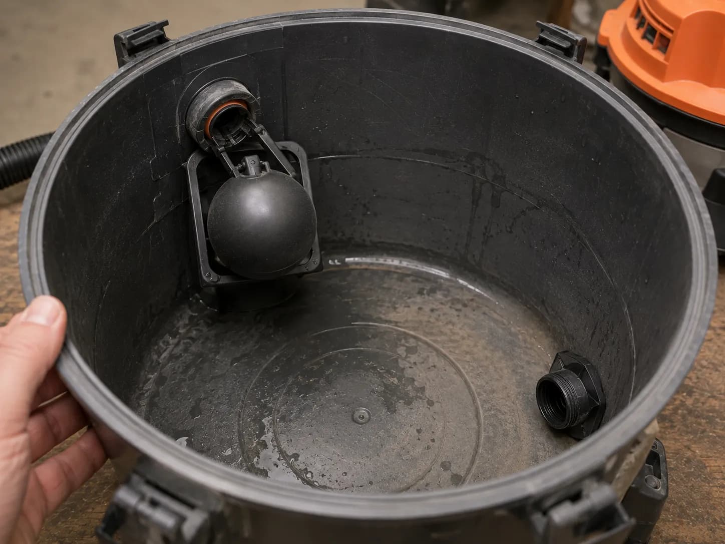 A float valve and drain port inside a shop vac tank that mark a wet-capable machine.